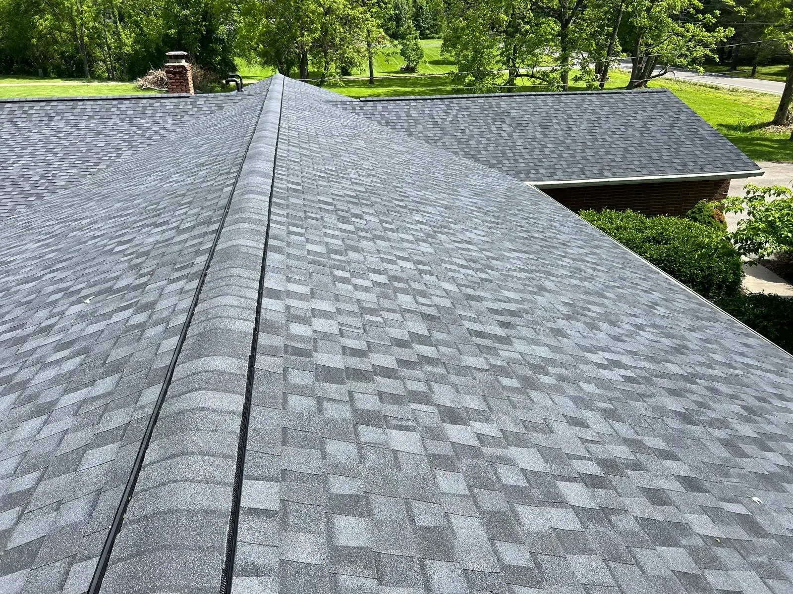 Sensational Roofing Services In Brookville, OH | Maxim Roofing A close-up photo taken from on top of a gray shingled, low-slope residential roof. There are green trees in the background of the picture, beyond the house.